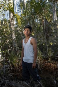 Luis Angel Saire Collo poses for a portrait inside the aguajal (tropical palm tree peatlands) in Bello Horizonte. Luis Angel lives and works in Bello Horizonte, an Ecotourism complex located next to one of the largest and still virgin aguajales (tropical palm tree peatlands) in the area. For some years now, the Amazonian area of Madre de Dios in Peru has been impacted by legal, illegal, and informal gold mining. To tap the gold, miners literally turn the jungle upside down. They arrive in a humid, leafy, abundant territory and leave behind a desert, often contaminated by mercury, a fundamental element for gold mining. Madre de Dios, Peru. Photographer: Luján Agusti. July 2022.